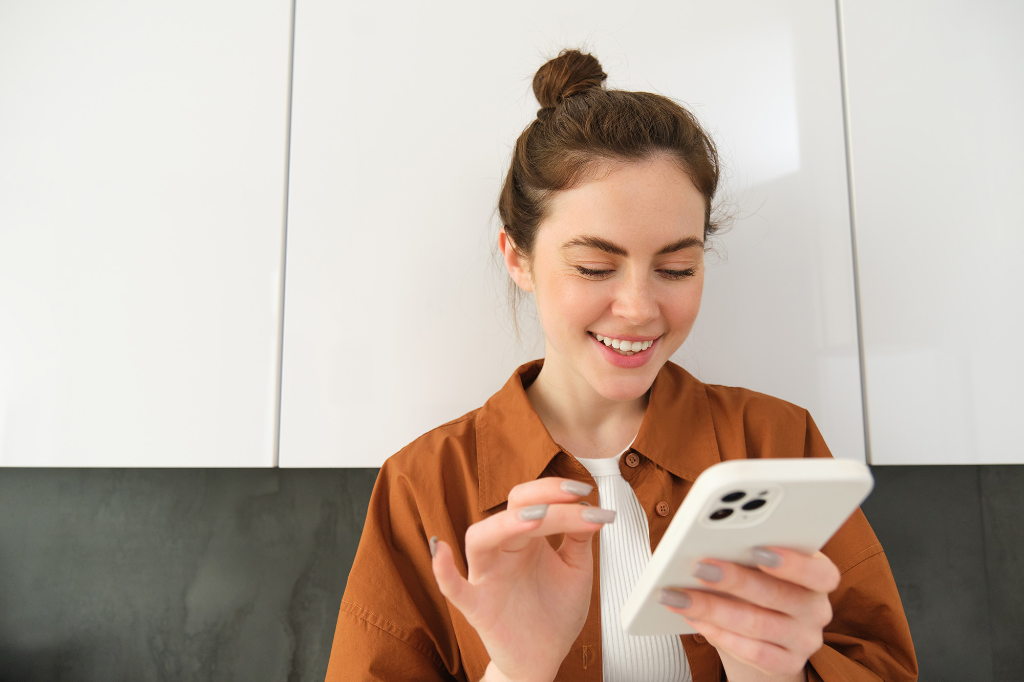 happy-girl-with-smartphone-looking-phone-smiling-standing-home-concept-buying-online